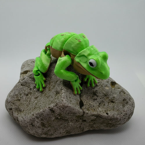 L3D Prints articulated green frog toy with brown accents, detailed limbs and eyes, perched on a rock.